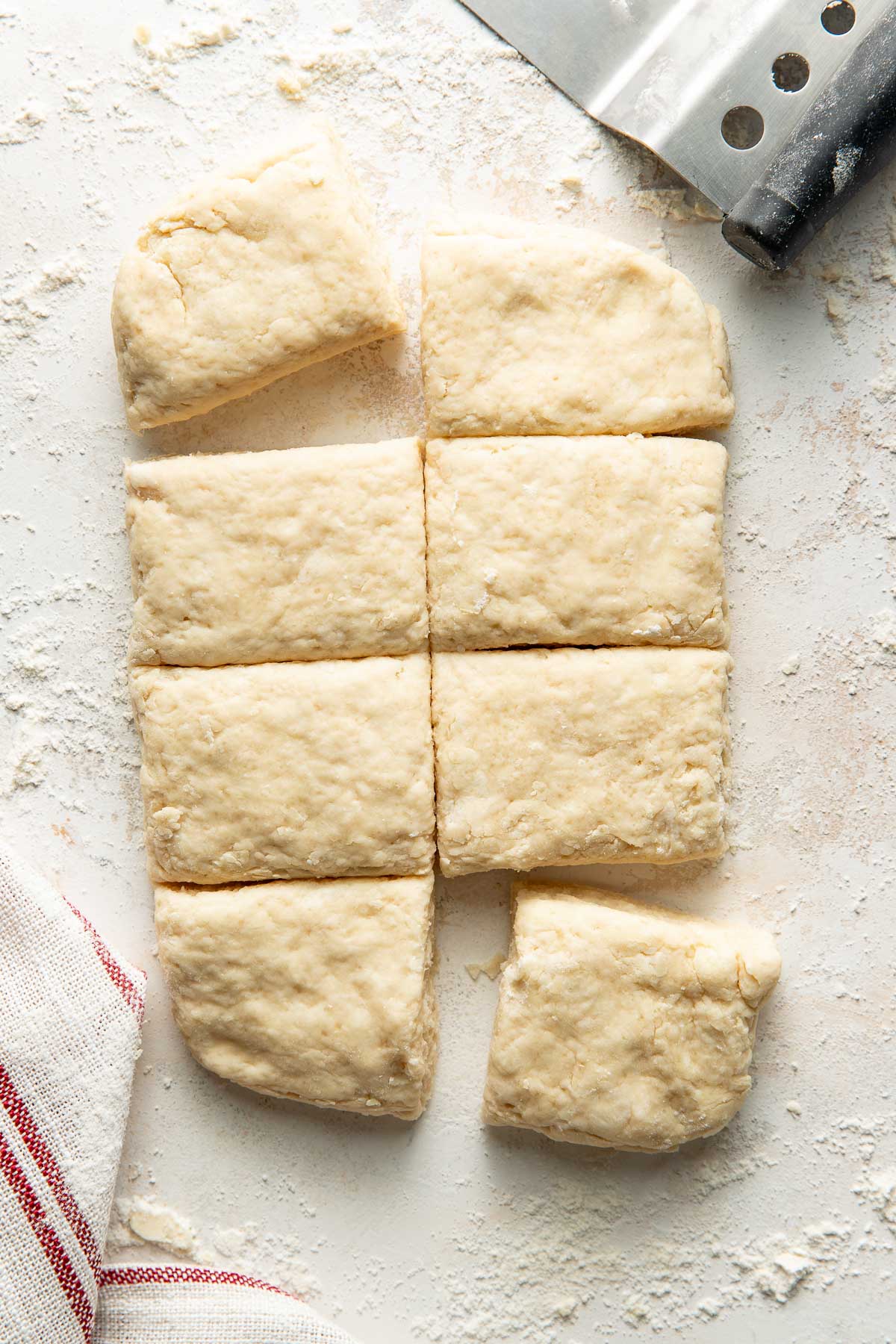 Overhead view of a piece of sweet cream biscuit dough cut into eight squares on a floured countertop
