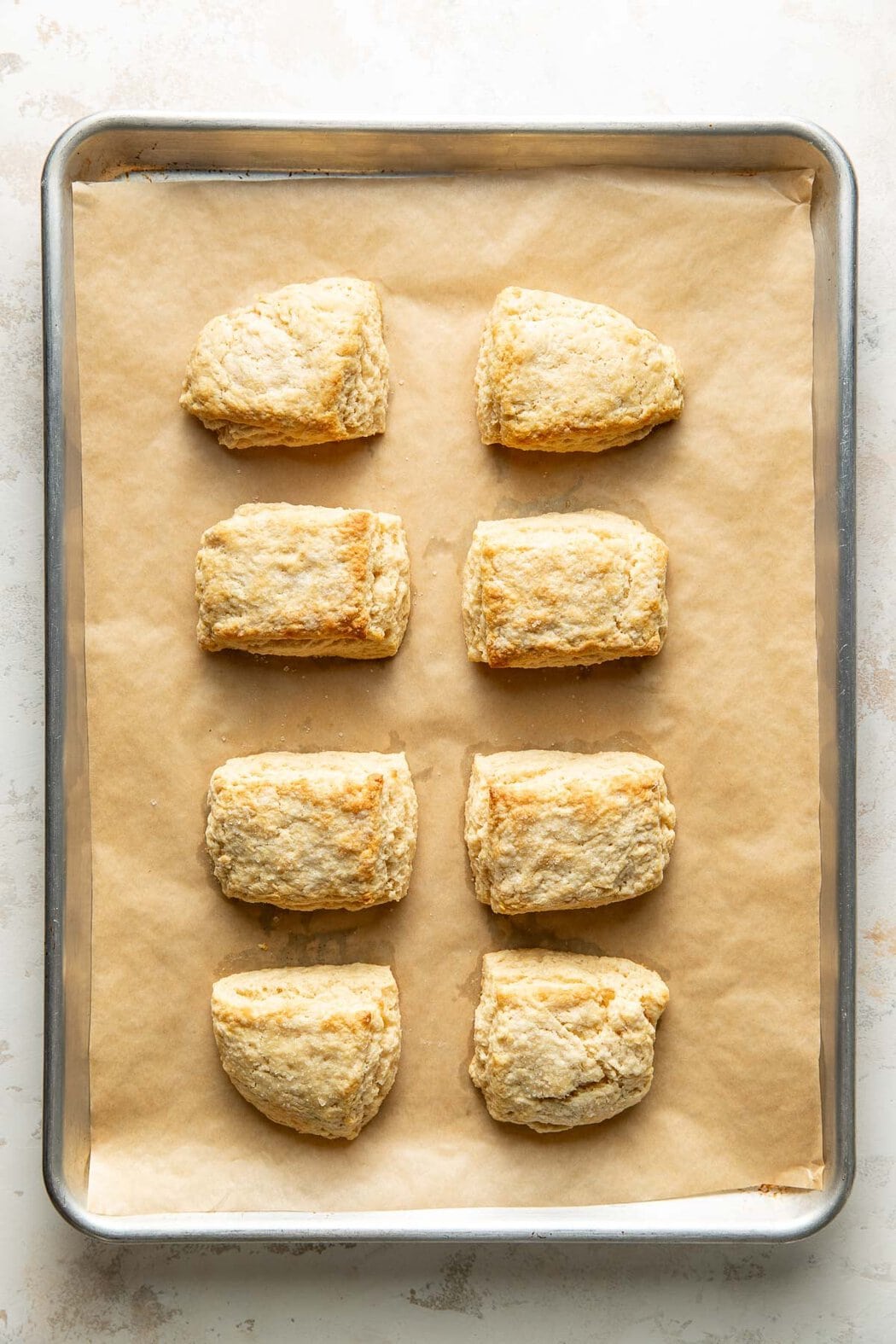 Overhead view of a parchment lined sheet pan filled with eight squares of biscuits.