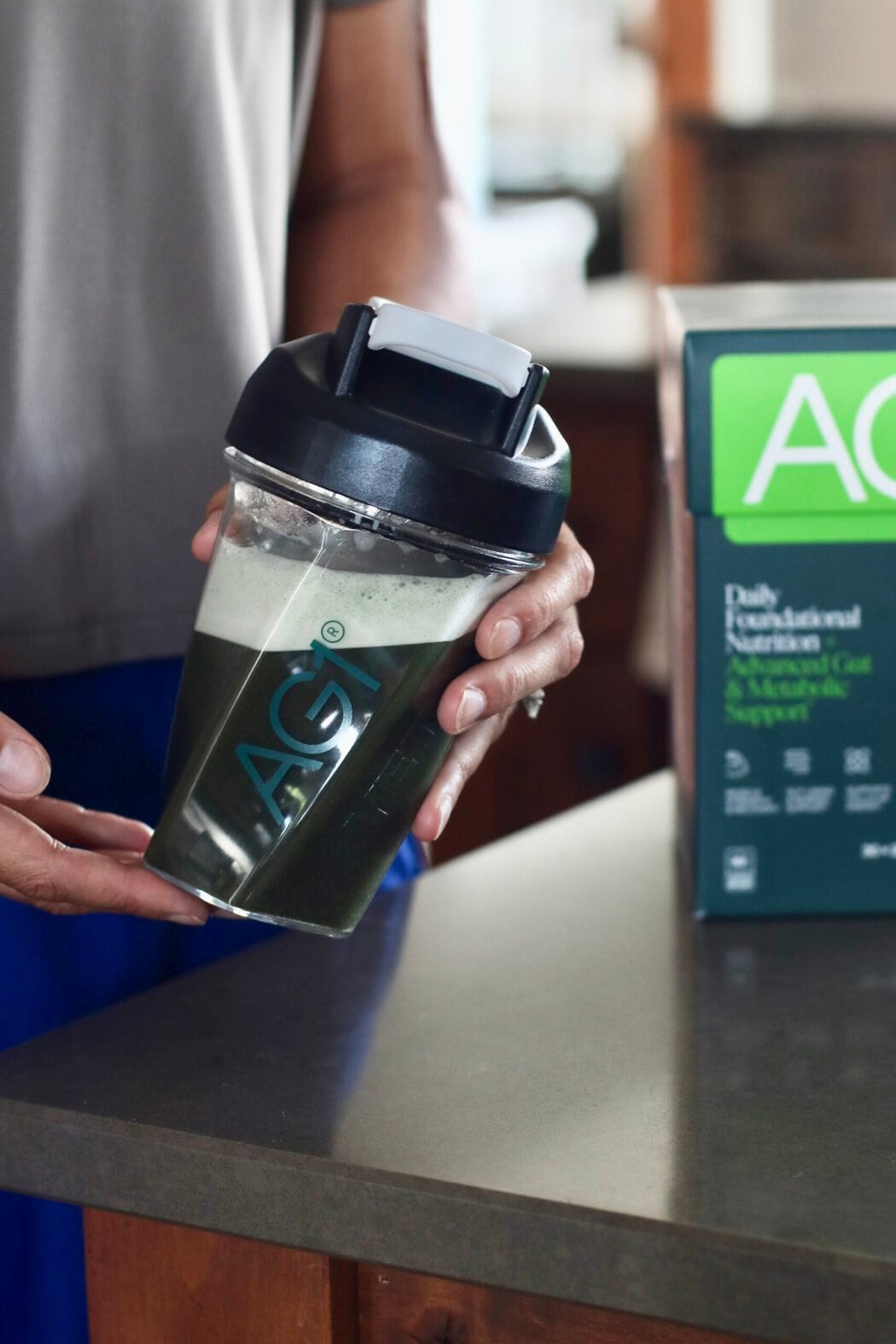 A woman holding an AG1 shaker bottle full of water and a shaken AG1 Pro packet. 