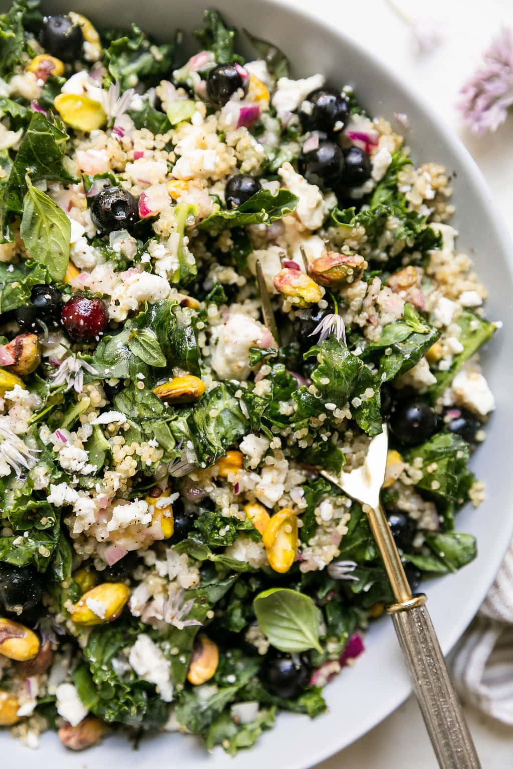A kale quinoa salad with lemon vinaigrette dressing in a bowl, a fork sticking out of the center. 