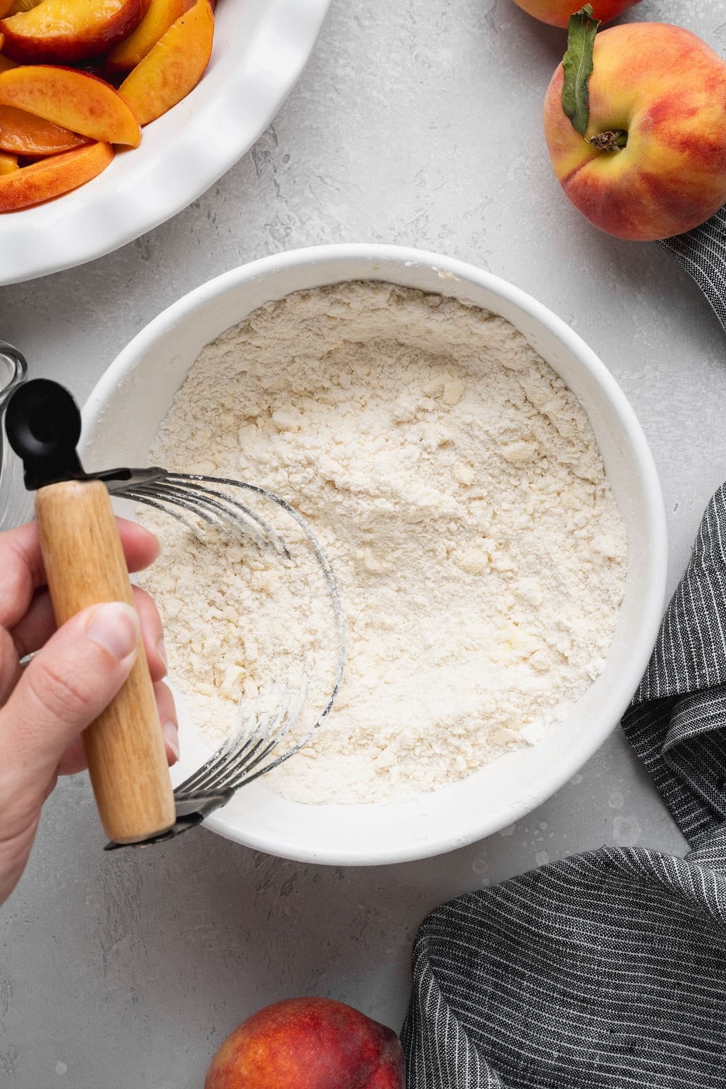 A hand using a pastry cutter to cut cold butter into a bowl of flour to make pastry dough.