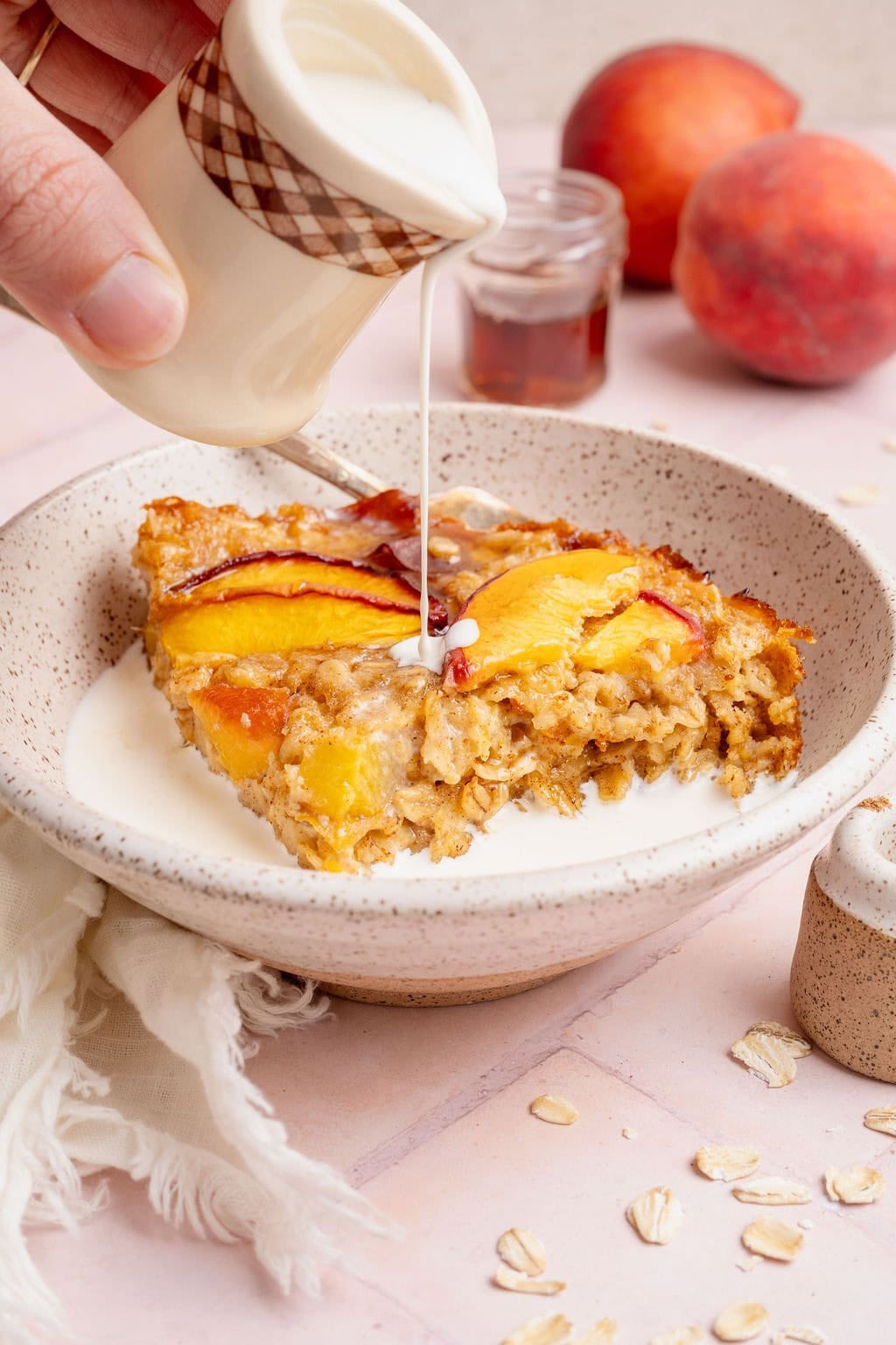 A serving of peaches and cream oatmeal in a bowl with a hand pouring heavy cream on top.